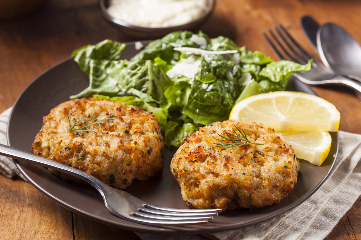 Two crab cakes served on a plate with salad and lemon slices