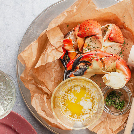 Stone crabs on a paper-lined plate with butter, herbs, and a George Stone Crab wooden mallet