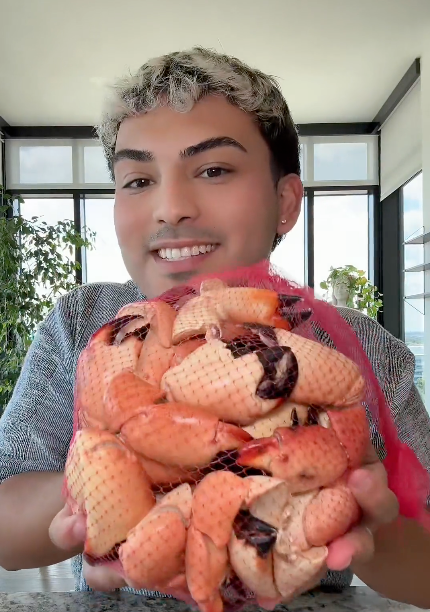 A person holding a large mesh bag filled with peeled shrimp claws, photographed indoors in front of large windows.