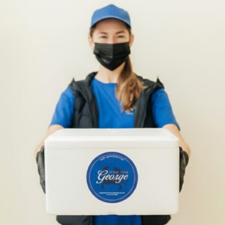 Person wearing a blue cap and face mask, holding a white box with a 'Team George' logo.