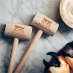 Two wooden seafood mallets with handles, placed on a marble surface with a dish of stone crabs in the background.